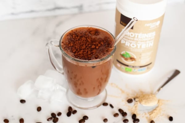 A glass full of a protein drink next to a container of protein powder