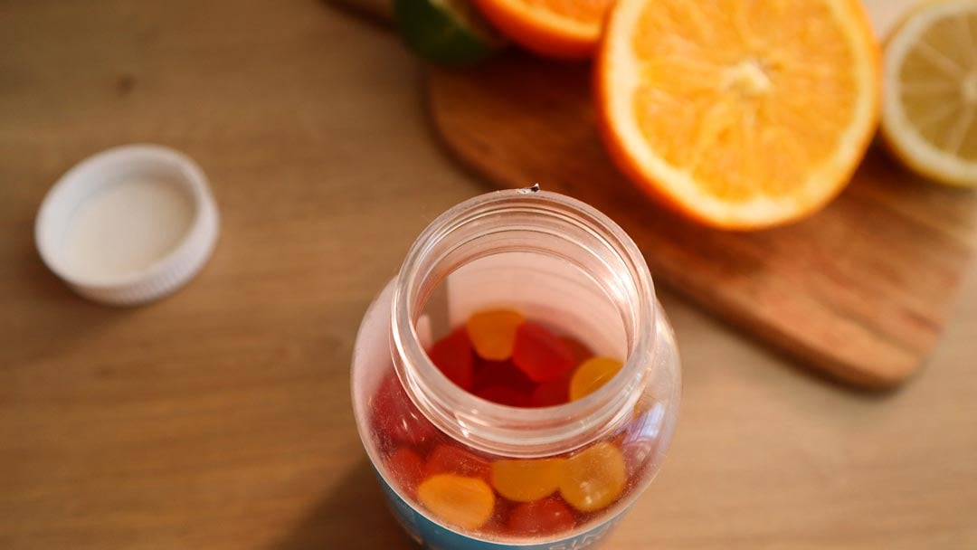 A bottle of gummy vitamins next to cut up oranges.